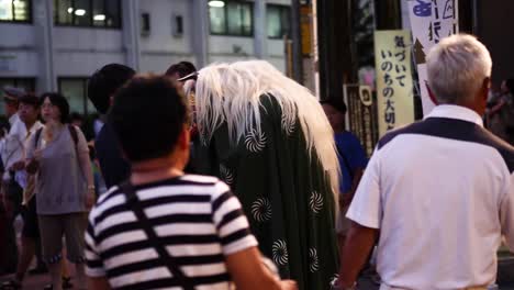 Traditional-Japanese-festival-in-the-countryside,-with-a-man-in-a-traditional-lion-costume-dancing-and-interacting-with-the-public,-and-taiko-drums-played-in-the-background