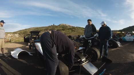 Mann,-Der-Die-Schraube-An-Der-Reifenfelge-Eines-Weißen-Rennwagens-Mit-Einem-Schraubenschlüssel-Auf-Dem-Hügel-In-Imtahleb-Malta-Zurücksetzt---Gopro-Pan-Shot