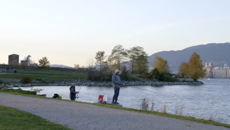 Amigos-Fueron-A-Pescar-Un-Fin-De-Semana-En-Un-Lago-Vancouver-Con-Vistas-A-Montañas-Y-Edificios-Altos-Antes-De-La-Puesta-Del-Sol---Plano-General