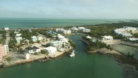Aerial-View-of-Resort-and-Neighborhood-on-Knight's-Key-in-Marathon-Florida-With-Fishing-Boat-and-Palm-Trees-Blowing-in-Wind-and-Ocean-in-Background-Tracking-Forward