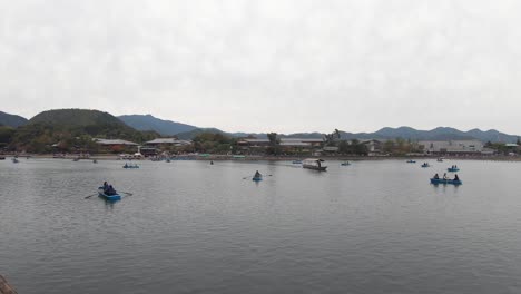 Tourists-under-overcast-sky-enjoy-Katsura-River-by-rowboat,-Kyoto