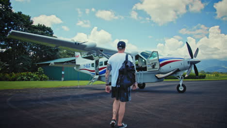 4k-Zeitlupen-Rückaufnahme-Eines-Reisenden-Mit-Hut-Und-Rucksack,-Der-Zuversichtlich-In-Richtung-Eines-Charterflugzeugs-Auf-Dem-Flugplatz-Aufwacht