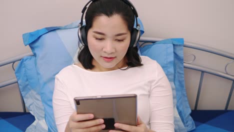 Fröhliche-Junge-Schöne-Asiatin,-Die-Sich-Entspannt-Und-Musik-Per-Tablet-Mit-Kopfhörern-Auf-Dem-Bett-Zu-Hause-Lifestyle--Und-Vergnügungskonzept-Hört