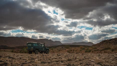 Lapso-De-Tiempo-De-Las-Nubes-Y-Los-Rayos-Del-Sol-Sobre-El-Vehículo-4wd-Estacionado-En-El-Desierto,-Gran-Angular