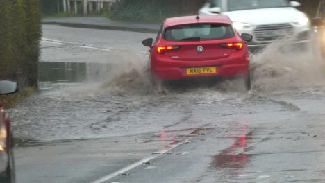 Vehicles-driving-on-stormy-splashing-flash-flooded-road-corner-bend-UK-closeup