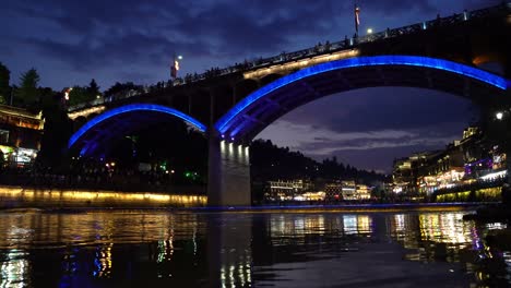 Illuminated-at-night-old-historic-arched-road-bridge-over-Tuo-river,-flowing-through-the-centre-of-Fenghuang-Old-Town,-China