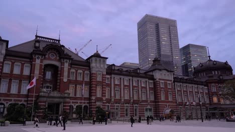 Abgesperrter-Seitlicher-Blick-Auf-Den-Bahnhof-Von-Tokio-Mit-Wolkenkratzern-Im-Hintergrund-Und-Menschen-Mit-Gesichtsmasken,-Die-Durch-Den-Rahmen-Gehen