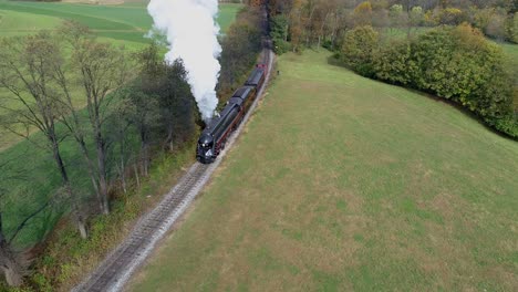 Aerial-view-of-an-antique-restored-steam-locomotive-traveling-thru-countryside-as-it-is-blowing-white-smoke-and-steam