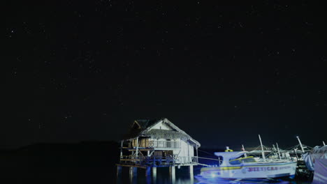 Estelas-De-Estrellas-Frente-Al-Océano-Con-Una-Cabaña-De-Nipa-Y-Barcos-Atracados