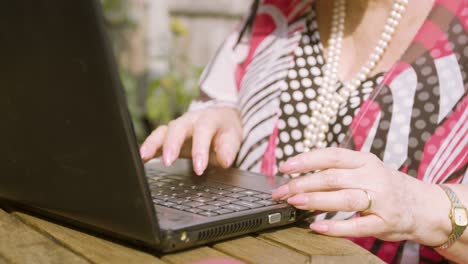 Elderly-Woman-close-up-on-her-hands-typing-on-a-black-laptop-outside