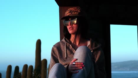 Retrato-Mujer-Puesta-De-Sol,-Joven-Latina-Mirando-El-Sol-A-La-Luz-Del-Atardecer-Con-Sombrero-Y-Gafas-De-Sol,-Chile,-Pichilemu,-Punta-De-Lobos,-Playa-De-Surf