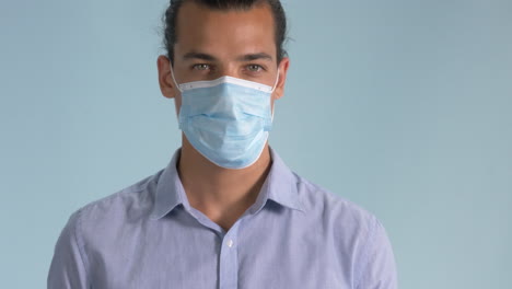A-Good-Looking-Man-Putting-On-A-Surgical-Mask-Isolated-On-Light-Blue-Background---Covid-19-Outbreak---Closeup-Shot
