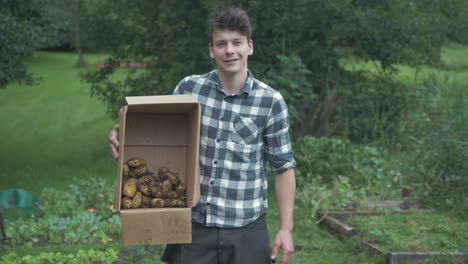 Junger-Männlicher-Kaukasischer-Gärtner-Hält-Eine-Kiste-Mit-Biologisch-Angebauten-Kartoffeln-In-Der-Hand-Und-Lächelt-Stolz