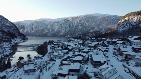 Fliegen-In-Der-Nähe-Von-Häusern-In-Der-Verschneiten-Stadt-Stanghelle---Vorwärtsbewegte-Antenne-Gegen-Fjord,-Berg,-Brücke-Und-Sonne