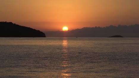 Sunset-from-Vela-Luka,-Croatia,-with-the-sun-partially-concealed-by-low-clouds-with-islands-in-the-foreground
