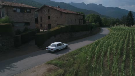 Toma-Aérea-De-Un-Automóvil-Bmw-E30-Conduciendo-Por-Una-Carretera-Rural