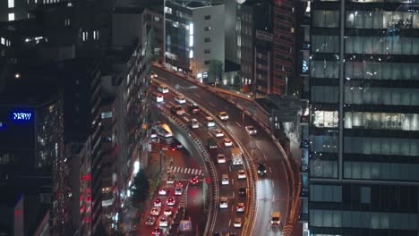 Tráfico-Pesado-En-La-Carretera-Con-Un-Edificio-De-Gran-Altura-En-La-Noche-En-Shibuya,-Tokio,-Japón