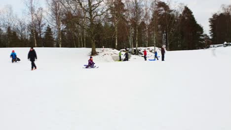 Girl-on-a-snow-racer,-sliding-down-a-snowy-winter-hill-with-plenty-of-people-around