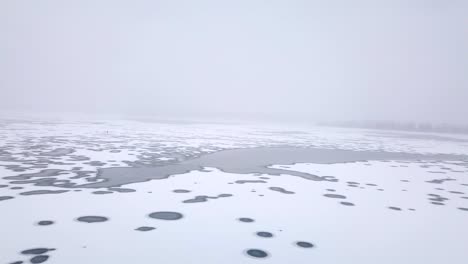 Eine-Fliegende-Weitwinkelaufnahme-Mit-Blick-Auf-Den-Zugefrorenen-Fluss-Während-Eines-Schneesturms