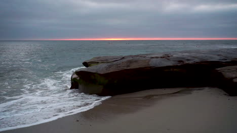 Las-Olas-Chocando-Contra-Una-Roca-En-La-Costa-De-San-Diego-Cuando-El-Sol-Se-Pone-Detrás-De-Las-Nubes-Oscuras