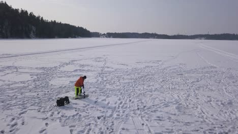 Wide-aerial-view-of-adult-male-preparing-a-fresh-hole-in-the-frozen-lake-to-enjoy-ice-fishing-on-a-beautiful-day