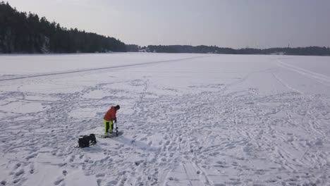 Große-Luftaufnahme-Eines-Erwachsenen-Mannes,-Der-Ein-Frisches-Loch-Im-Zugefrorenen-See-Vorbereitet,-Um-An-Einem-Schönen-Tag-Eisfischen-Zu-Genießen