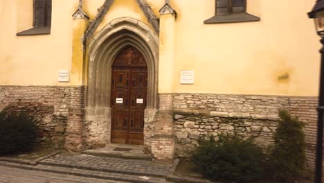A-trucking-low-level-drone-shot-capturing-the-entrance-and-windows-of-a-vintage-architectural-church-in-the-city-of-Sighisoara-on-an-afternoon
