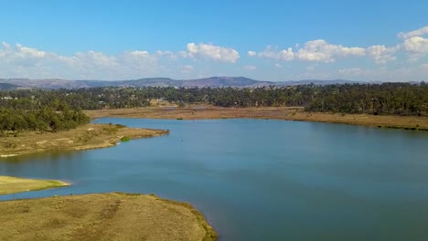 Drohnenaufnahmen-Bewegen-Sich-30-Meter-über-Dem-Wasserspiegel-Von-Links-Nach-Rechts-Und-Zeigen-Den-Färbersee-Mit-Einem-Schwarm-Weißer-Vögel,-Der-Aus-Dem-Bild-Fliegt