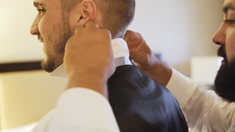 Groomsman-adjusting-the-groom’s-collar-in-a-hotel-room