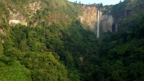 Sunny-approach-drone-shot-of-cliffs,-jungle,-and-Sipiso-Piso-waterfall-in-North-Sumatra,-Indonesia