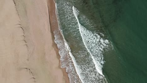 Small-beautiful-waves-hitting-the-shore-at-the-beach---stationary-aerial-shot