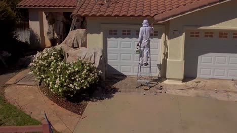 Aerial,-drone-shot,-of-person-working-on-painting-the-exterior,-of-a-house,-in-LA-suburbs,-in-Los-Angeles,-California,-USA