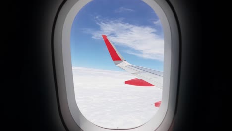 Blick-Auf-Einen-Roten-Flügel-Mitten-Im-Flug-Durch-Das-Runde-Fenster-Eines-Flugzeugs