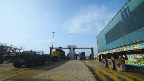 Trucks-entering-into-the-port,-A-long-vehicle-traller-is-moving-on-the-road-of-a-port,-camera-passing-close-up-and-tilting-down-view,-birds-flying-on-the-sky-while-truck-is-moving