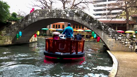 Die-Flussboote-Auf-Dem-San-Antonio-Riverwalk-Fahren-Ständig-Durch-Die-Innenstadt,-Deren-Bunte-Lichter-Auf-Der-Oberfläche-Zu-Tanzen-Scheinen