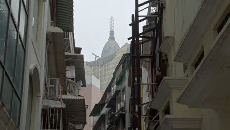 Top-of-Hotel-Grand-Lisboa-in-between-the-old-buildings-on-a-gray-overcast-day,-Macau,-Macau-SAR,-China