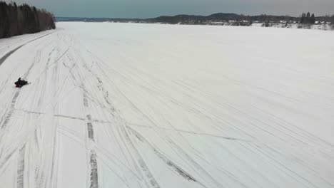 Tracking-aerial-shot-of-a-man-driving-his-snowmobile-on-Indalsalven-in-Timra,-Sundsvall,-Sweden