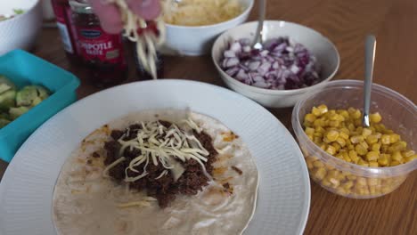 Putting-some-cheese-on-ground-taco-meat-laying-on-a-tortilla-bread