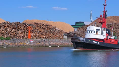 Black-and-red-colored-harbour-tug-leaving-Port-of-Liepaja-in-hot-sunny-day,-medium-shot