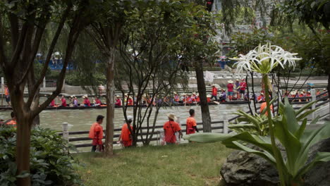 View-from-behind-the-trees-of-people-paddling-and-hitting-drums-on-a-dragon-boat-during-dragon-boat-festival-in-Guangzhou,-Guangdong-China