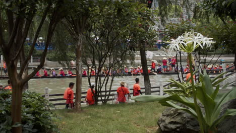 Vista-Desde-Detrás-De-Los-árboles-De-Personas-Remando-Y-Tocando-Tambores-En-Un-Bote-Dragón-Durante-El-Festival-Del-Bote-Dragón-En-Guangzhou,-Guangdong-China