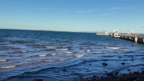 Langsame-Schwenkaufnahme-Eines-Woody-Point-Jetty-Mit-Meereswellen-An-Einem-Kalten,-Sonnigen-Morgen