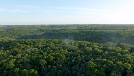Aerial-over-a-campground-on-a-densely-covered-forest-hill-while-smoke-is-coming-out-through-the-thick-foliage-indicating-barbecues-and-people-grilling-on-the-ground