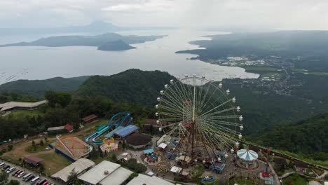 Vista-Aérea-De-Drones-Del-Parque-Temático,-Gran-Rueda-De-La-Fortuna-Del-Ojo-Del-Cielo-Y-Otro-Viaje-De-Aventura-En-La-Cima-De-La-Montaña