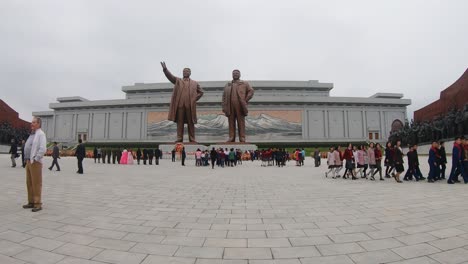 Nordkoreaner-Gehen-Am-Mansudae-Grand-Monument-Vorbei,-Während-Ein-Ausländischer-Tourist-Für-Ein-Foto-Posiert