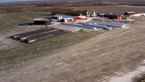 Vista-Aérea-De-Drones-De-Una-Estación-De-Paneles-Solares-Ligeramente-Cubierta-De-Nieve-Que-Alimenta-Una-Granja