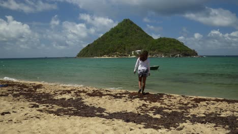 A-model-enjoying-a-walk-along-the-Caribbean-beach-Levera,-Grenada-with-an-island-in-the-background