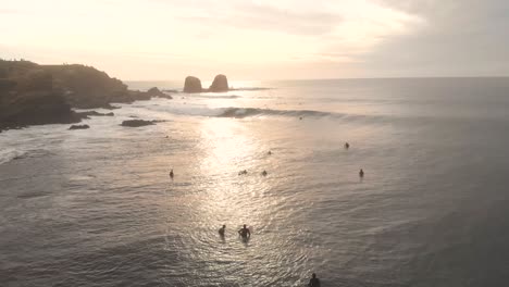 Aerial-drone-shot-at-the-sea-at-golden-hour-flying-above-surfers-with-giant-rocks-on-the-background,-Pichilemu,-Chile-4K