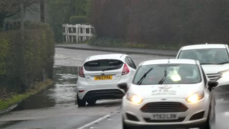 Car-stopping-to-let-vehicles-pass-on-stormy-flash-flooded-road-corner-bend-UK