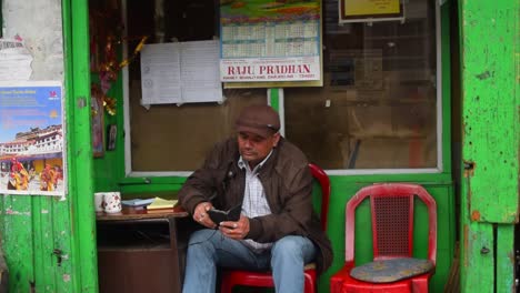 A-40-year-old-Indian-male-sitting-in-one-of-the-shops-in-the-Darjeeling-street-market-and-checking-his-phone